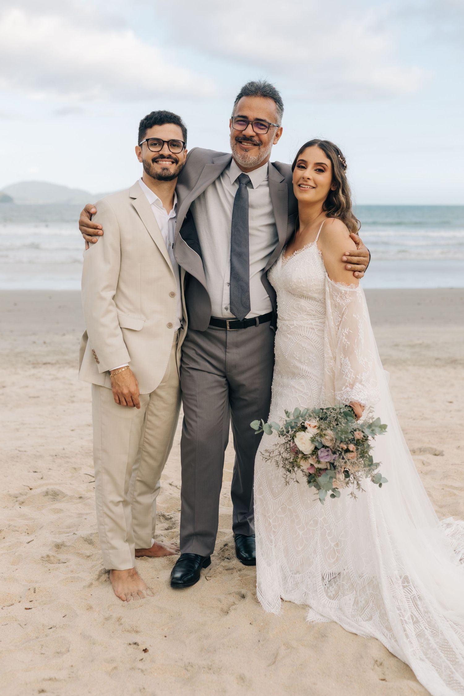 Wedding party members pose together on beach in formal attire.