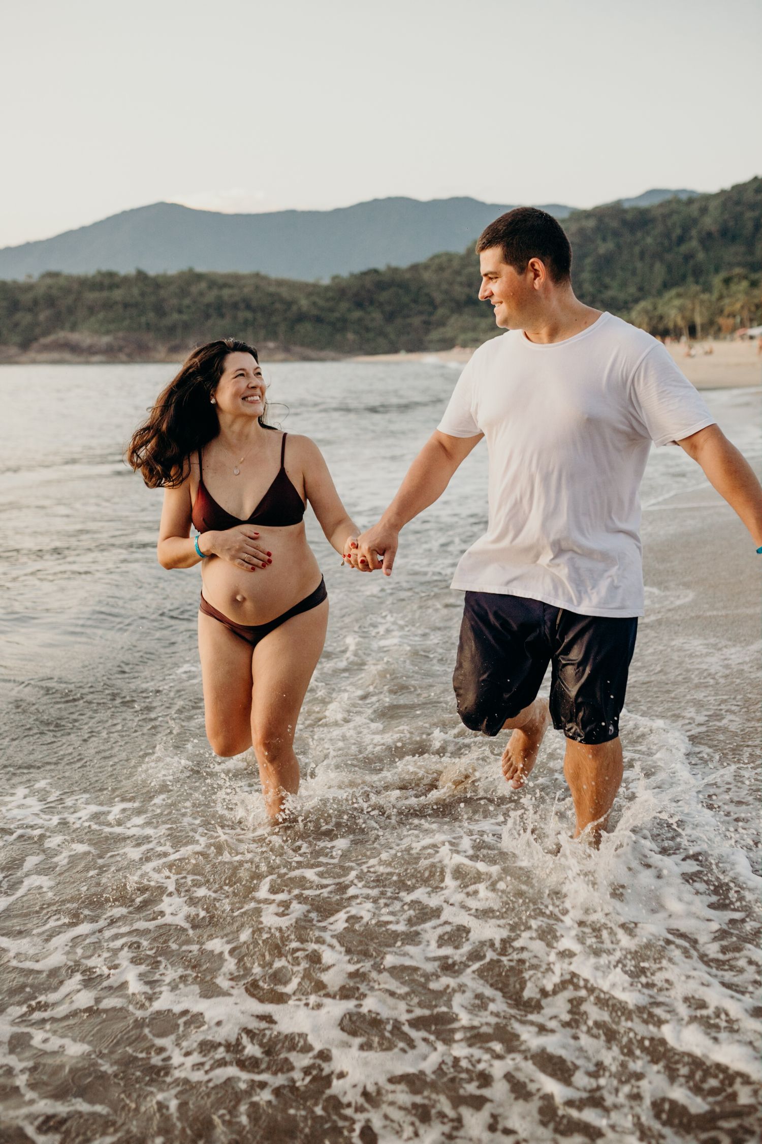 Couple splashing and laughing together in ocean waves at a scenic beach.