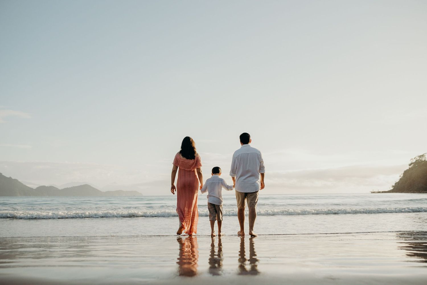 A family walks along a scenic beach at sunset holding hands while waves crash on the shore.