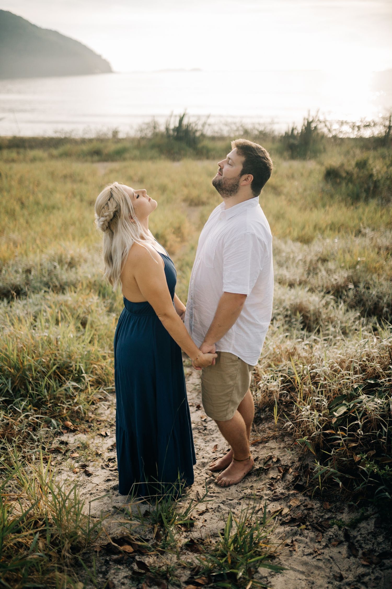 Couple sharing playful moment in golden sunlit field with natural backdrop.