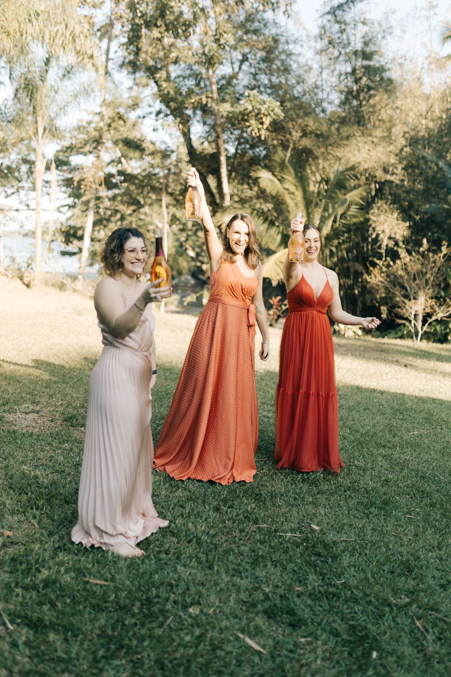 Group wearing gradient coral and beige dresses poses on grass under trees.