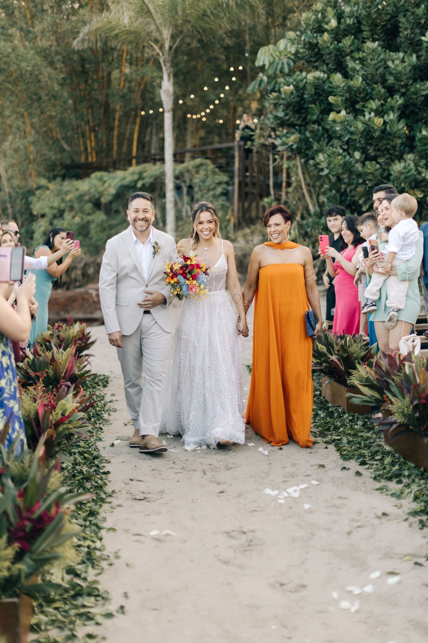 Wedding celebration on garden path with guests in light colored attire and string lights.