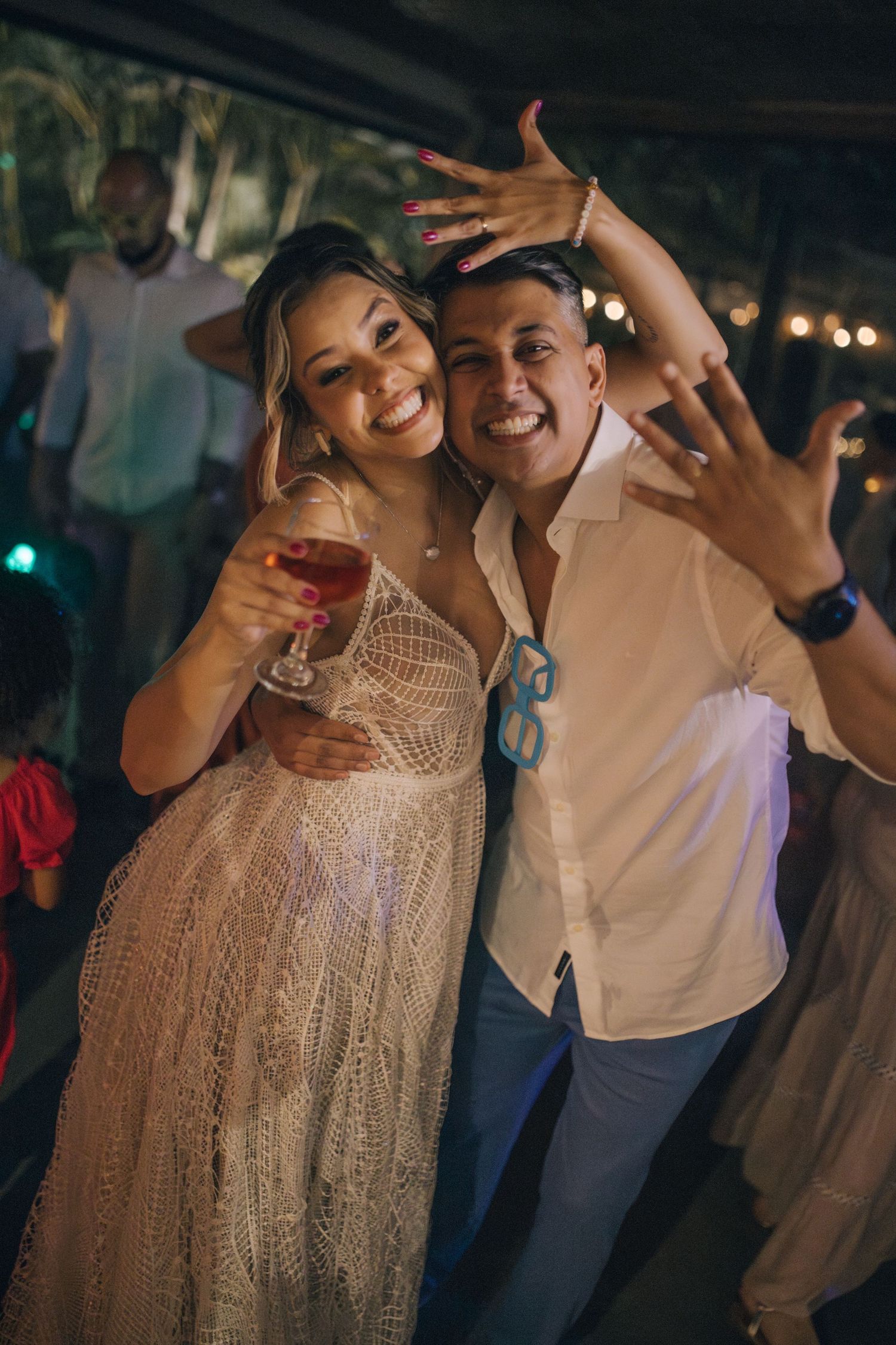 A fun reception moment with couple posing and making hand gestures while holding drinks.