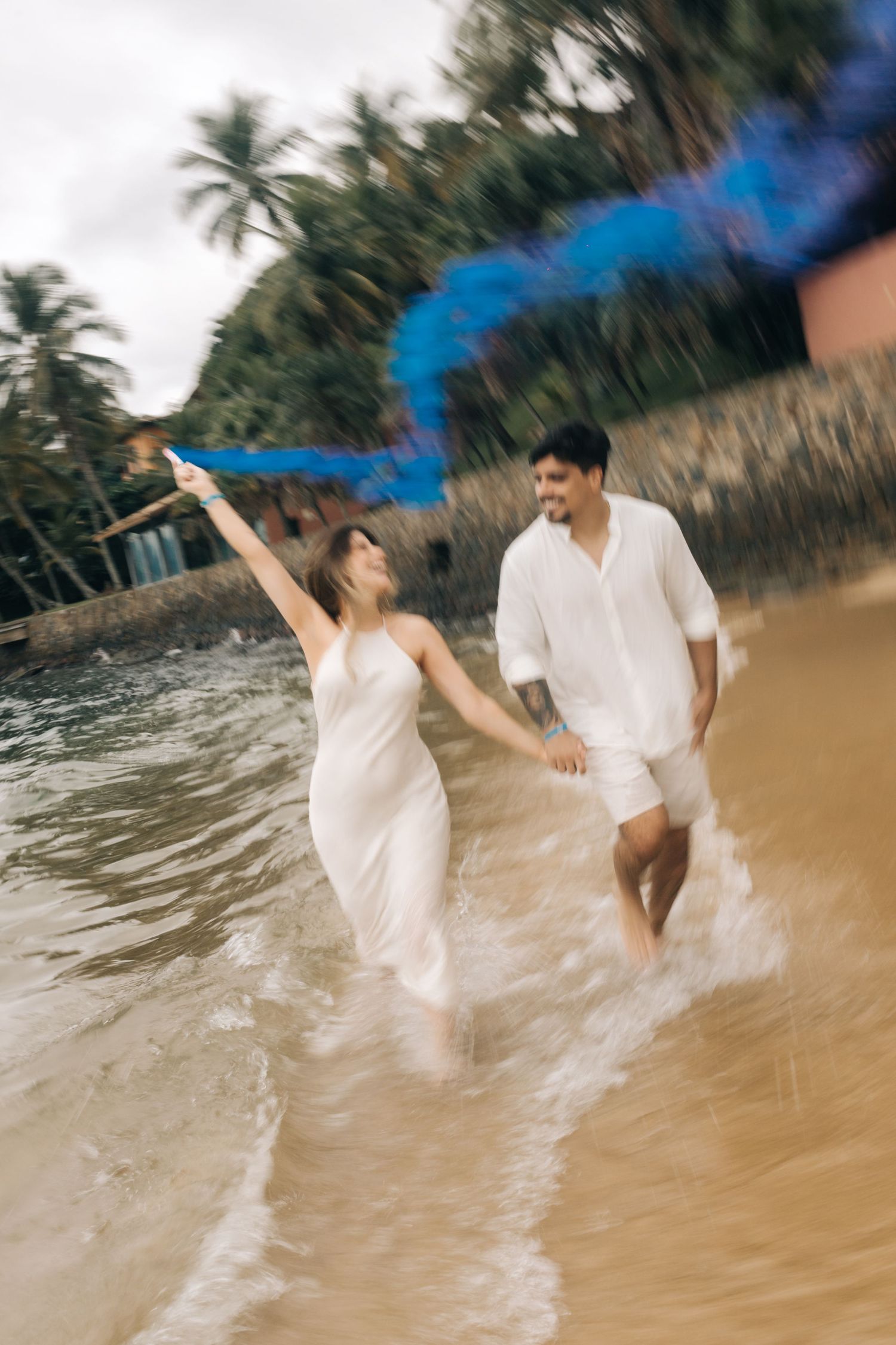 A couple plays with blue smoke bombs while splashing in the ocean waves.