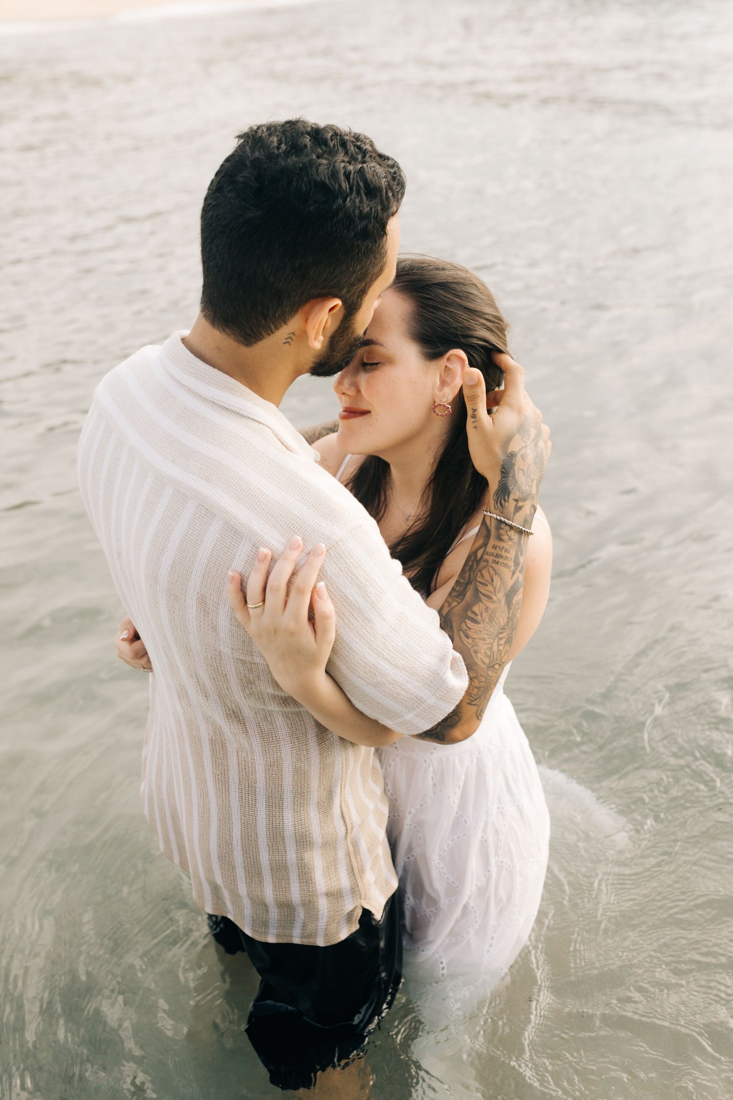 Two people embrace while standing in gentle ocean waves.