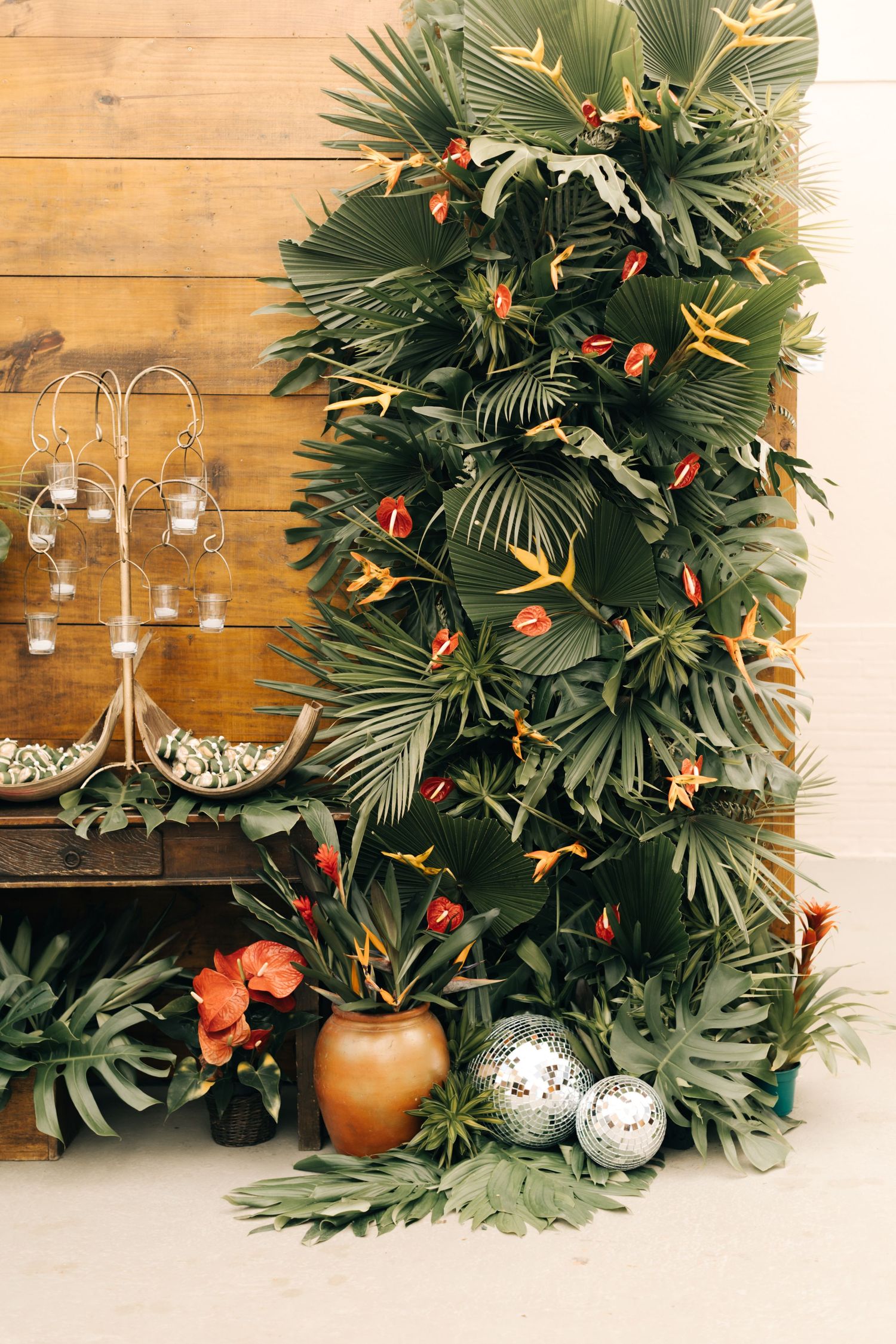 Dramatic tropical greenery wall display with palm leaves, orange flowers and metallic accents.