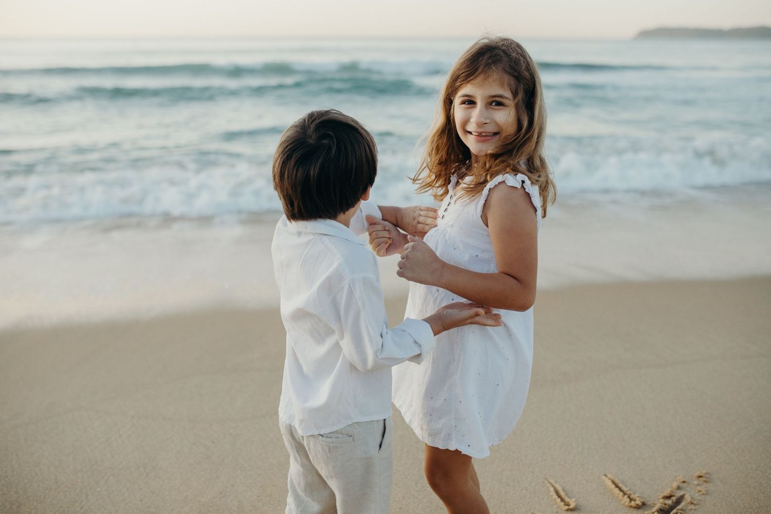 Two children sharing a sweet moment together on the beach at dusk.