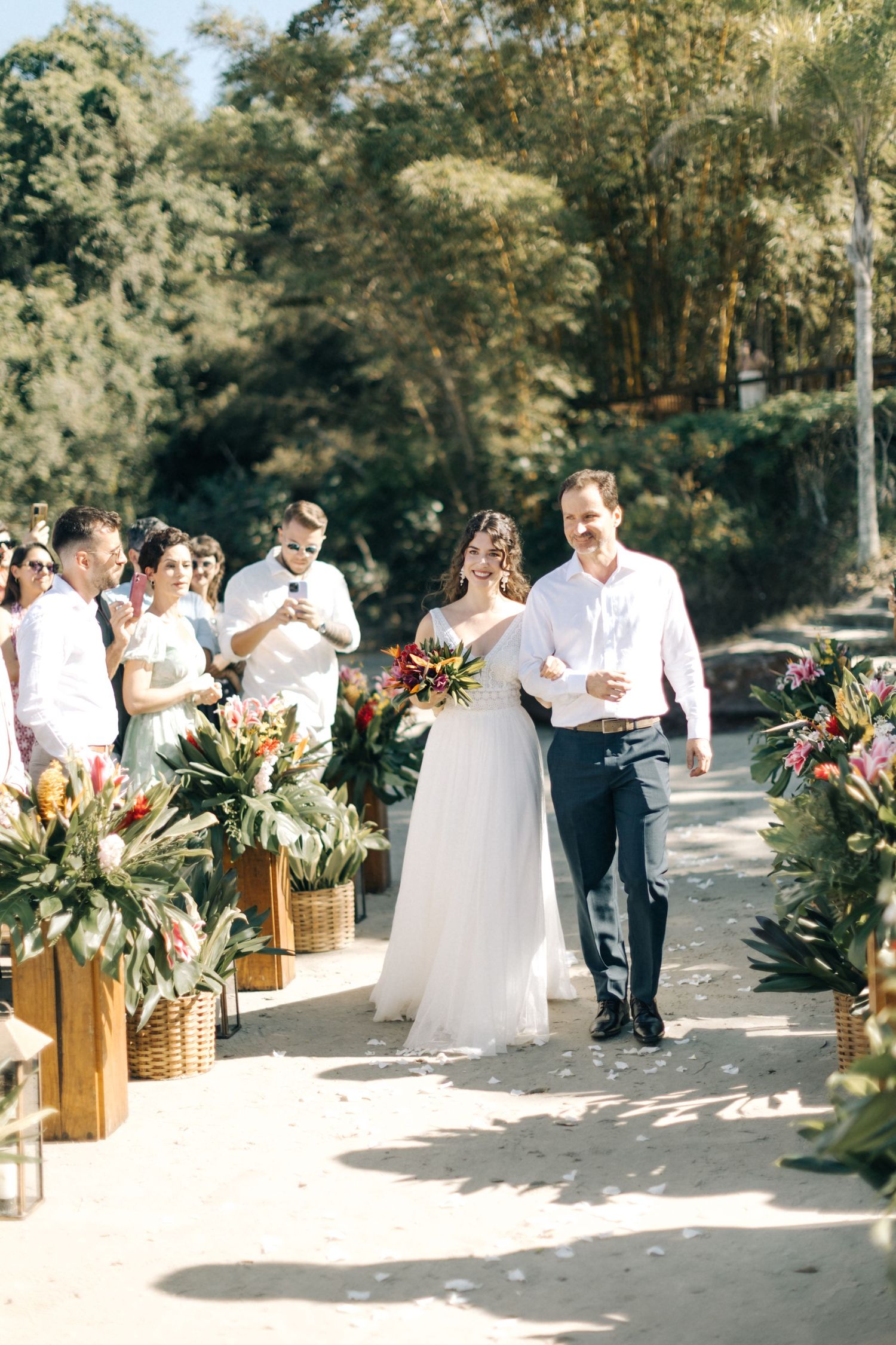 Outdoor wedding ceremony aisle decorated with tropical floral arrangements on wooden stands.
