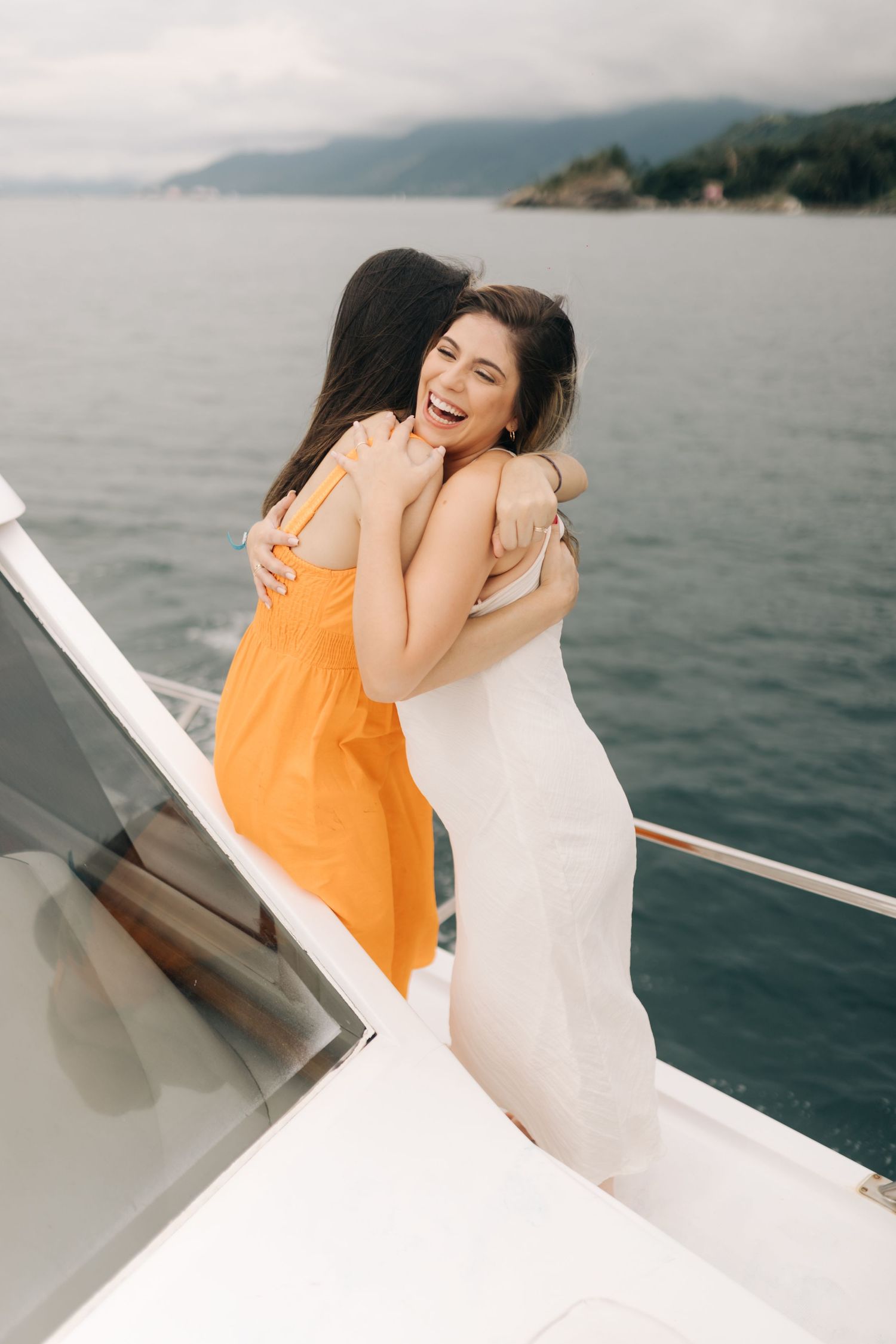 Candid moment of laughter and embraces on a yacht with scenic mountain views.