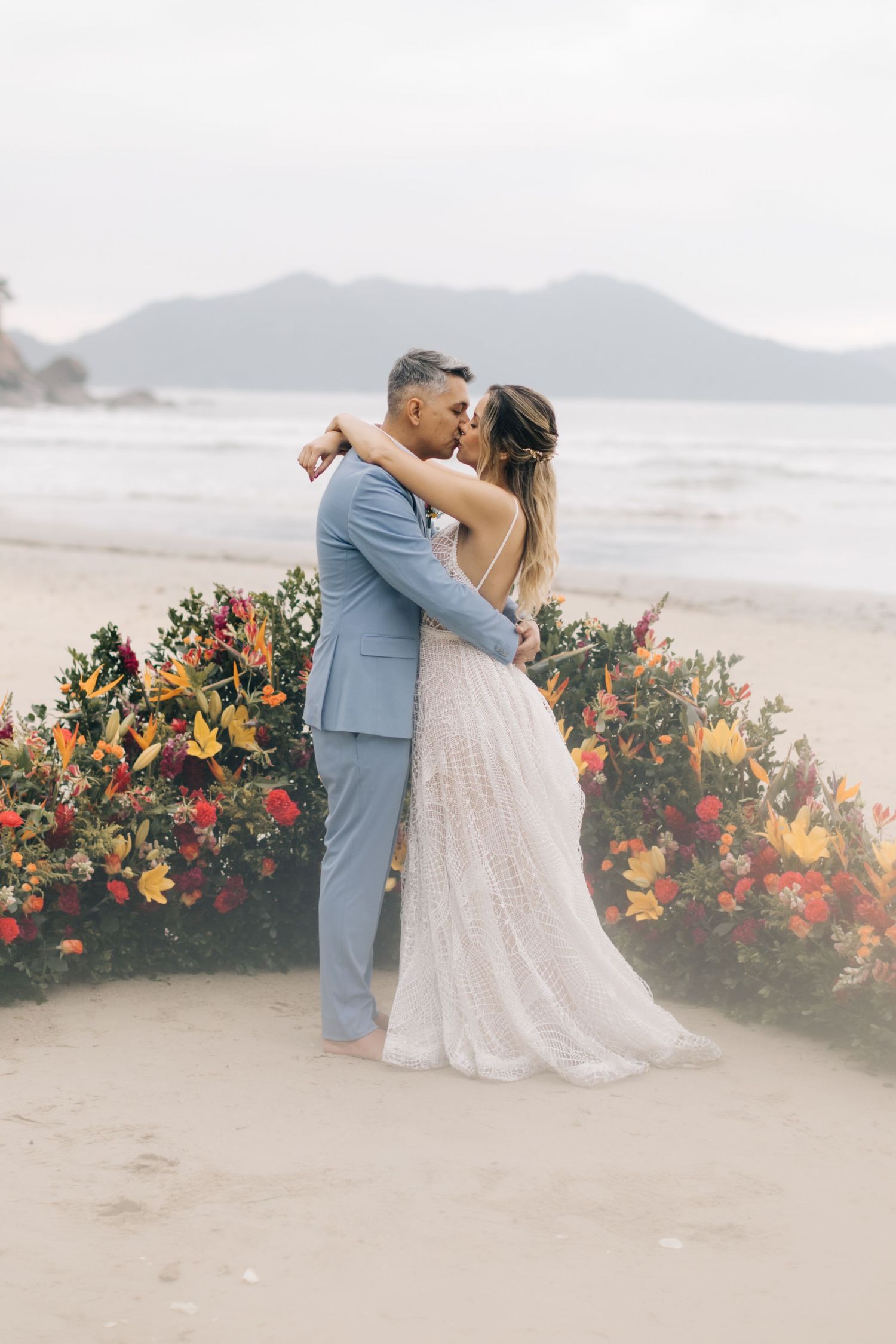 Romantic beach wedding portrait with couple embracing among colorful floral arrangements.
