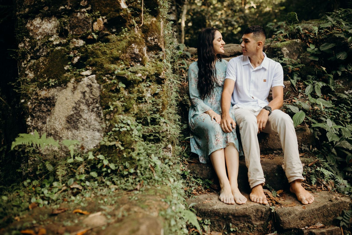 Couple sitting barefoot on stone steps surrounded by lush greenery and natural scenery.