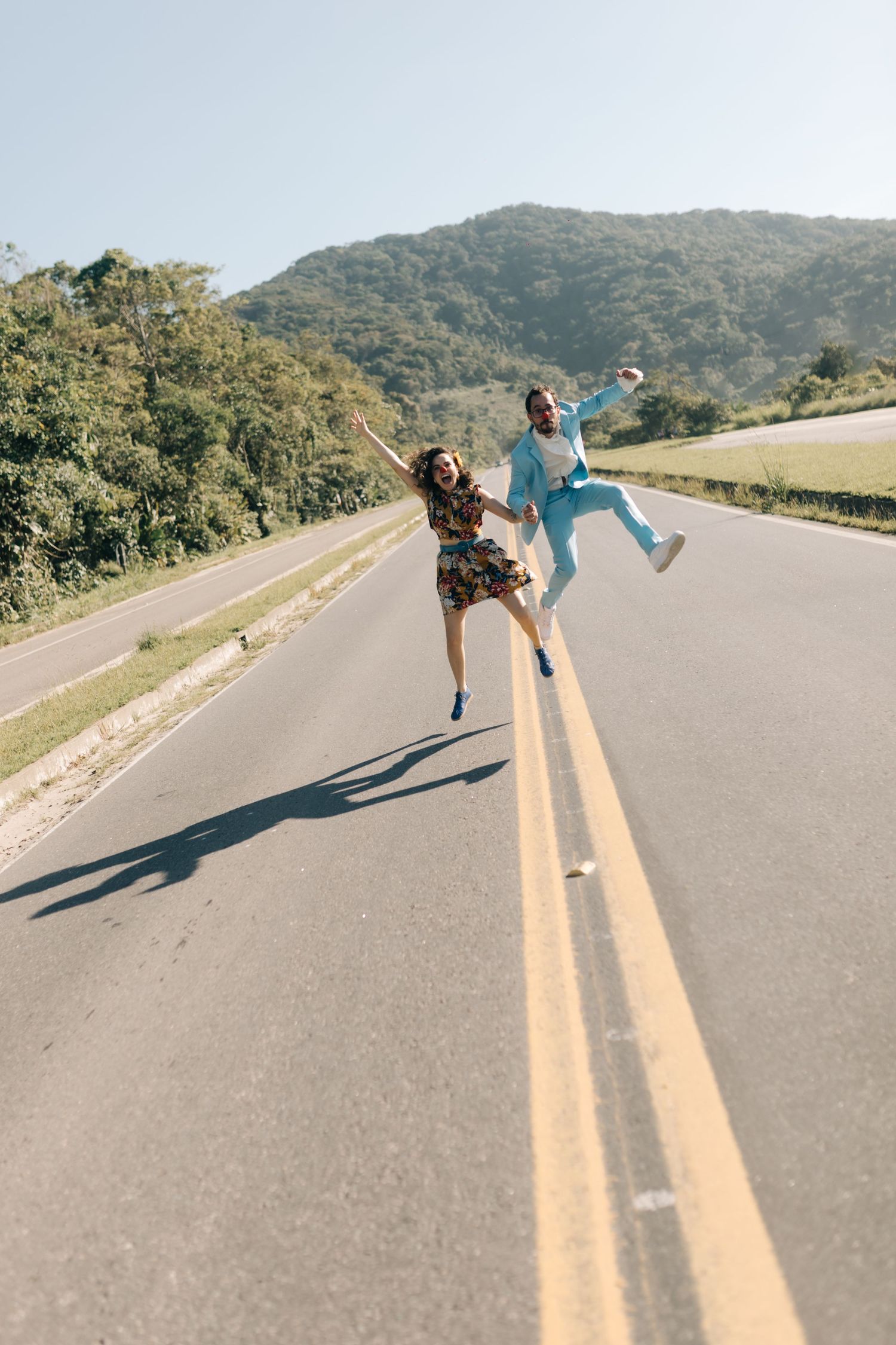 Energetic couple jumping on empty mountain road during sunny day.