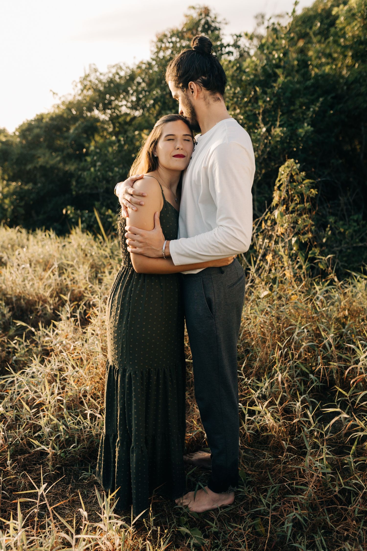 Loving embrace captured during golden hour engagement session in field.