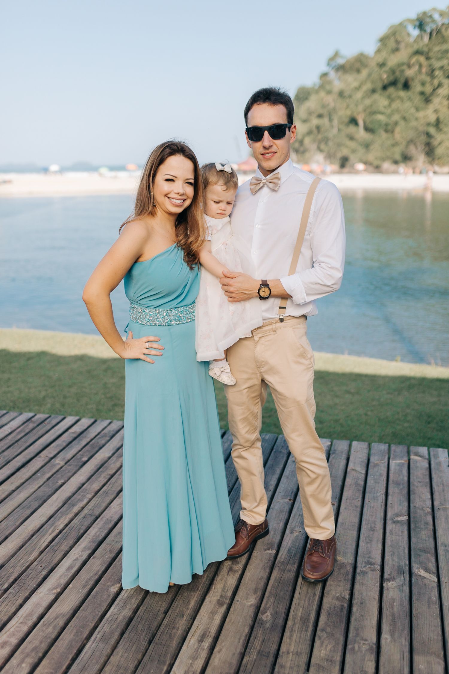 Family members in turquoise and khaki outfits pose on a wooden dock by a scenic lake.