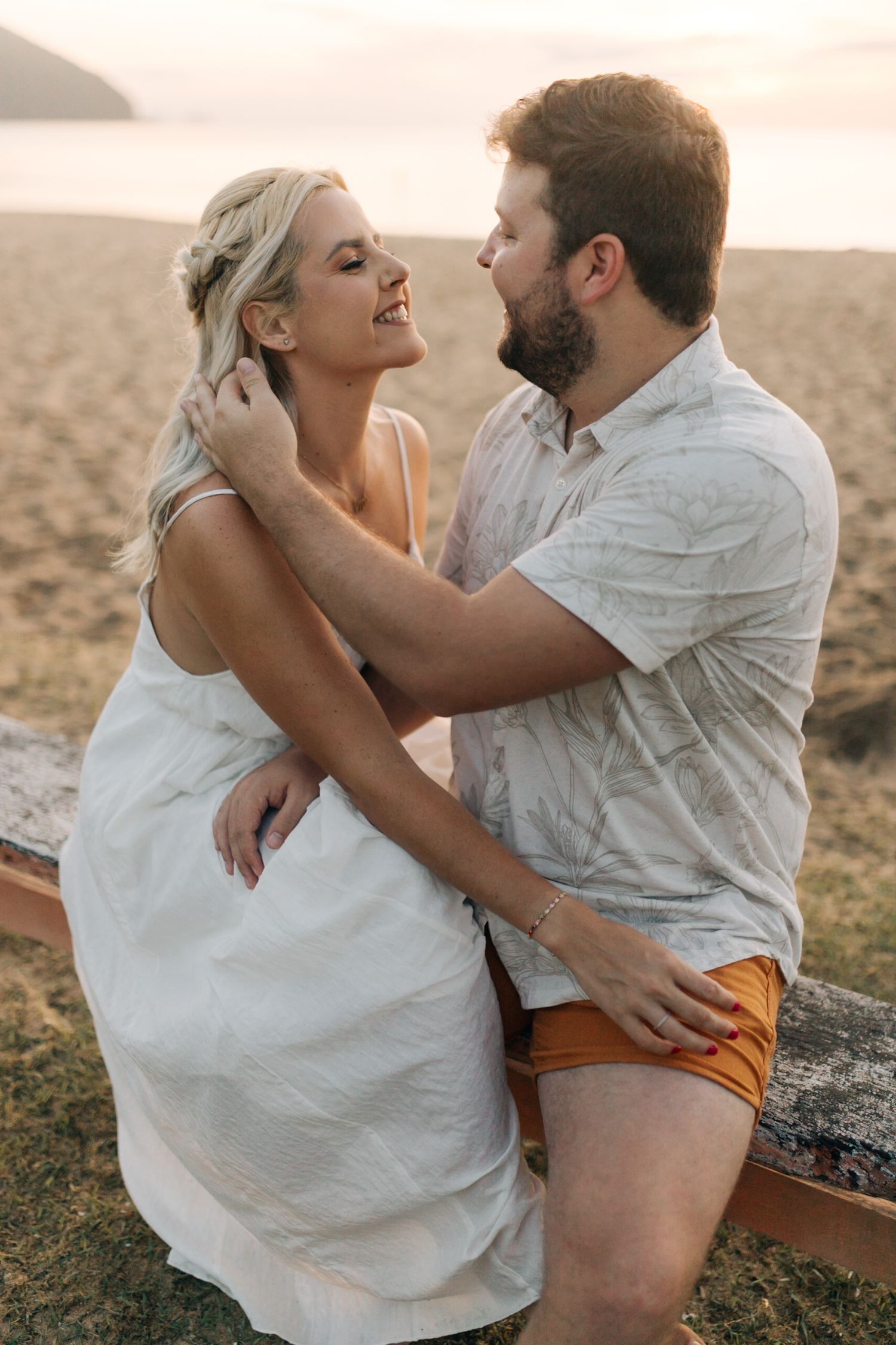 A tender embrace between a couple sitting on a wooden bench by the ocean at sunset.