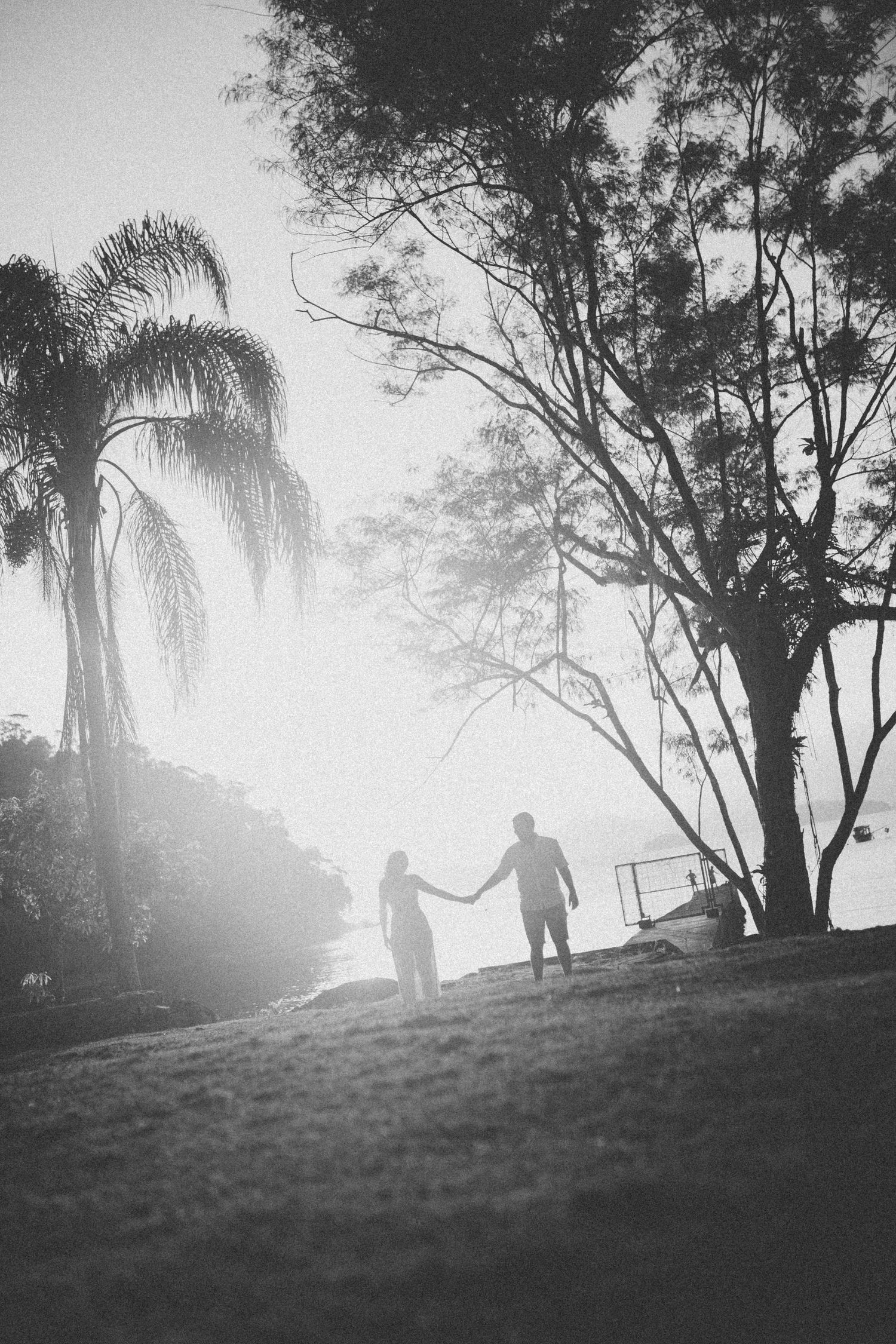 Black and white silhouette of a couple holding hands against palm trees and sunset sky.