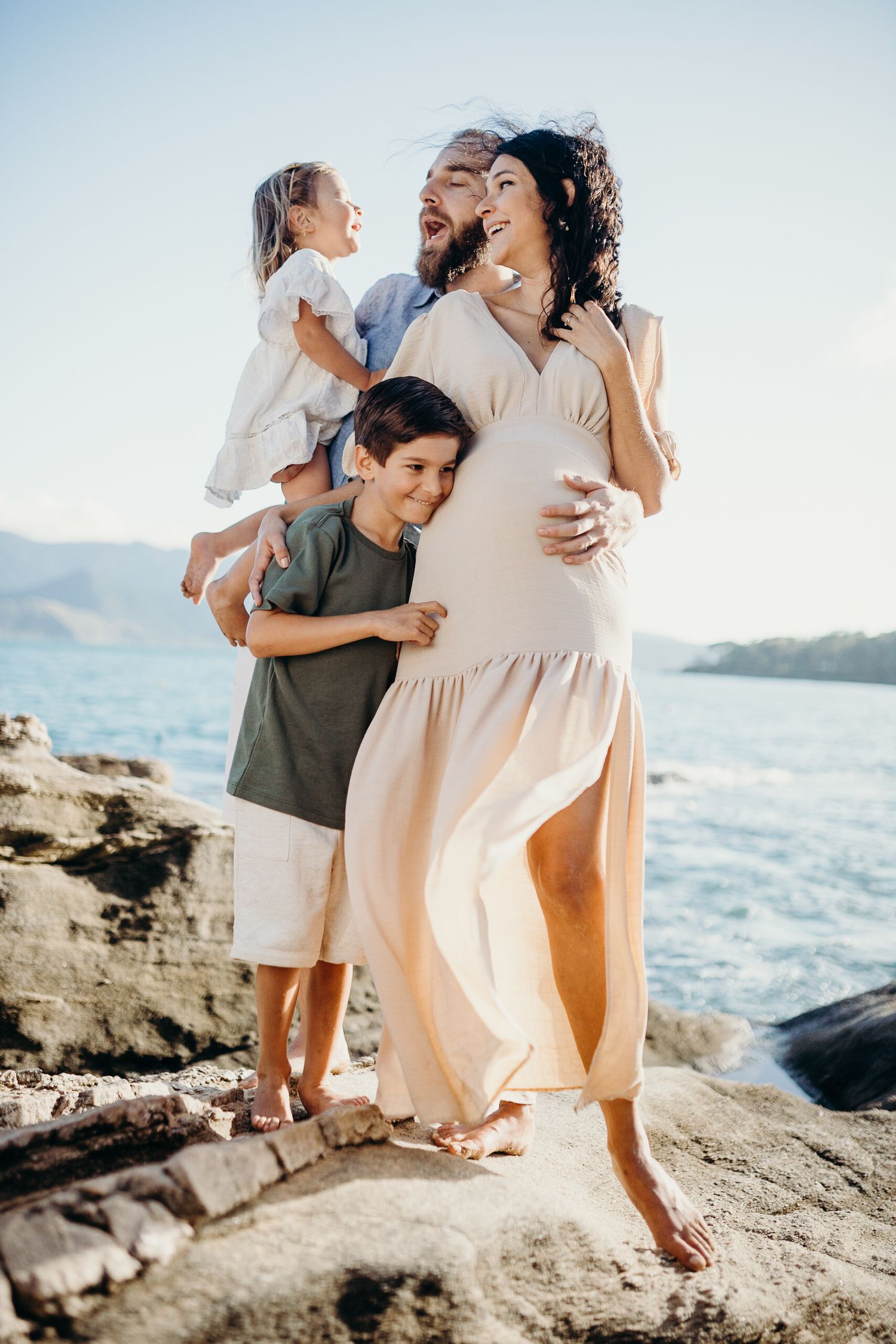 Family members share playful moments on rocky beach during sunset photo session.