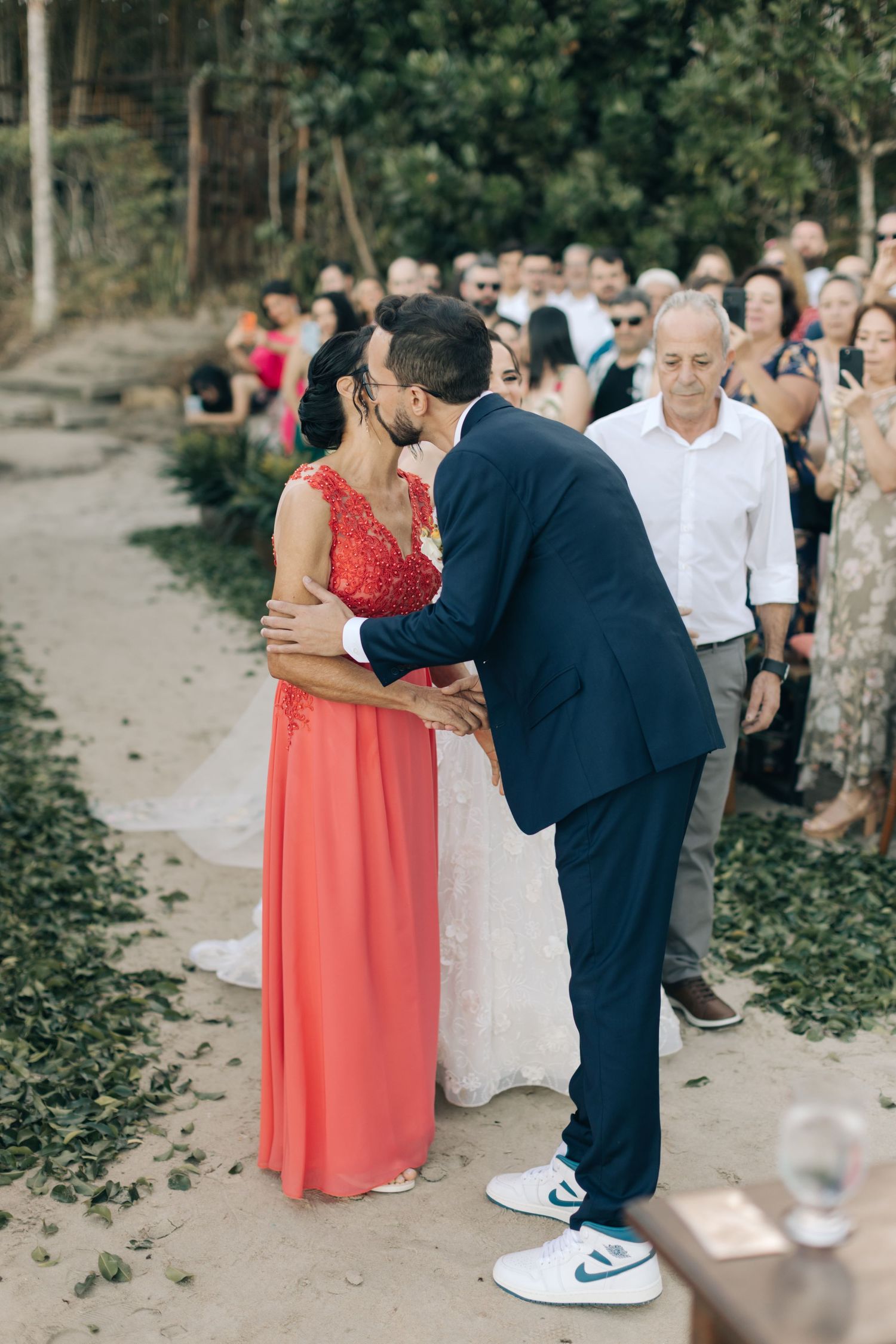 Wedding guests gather on a sandy path during an outdoor ceremony.