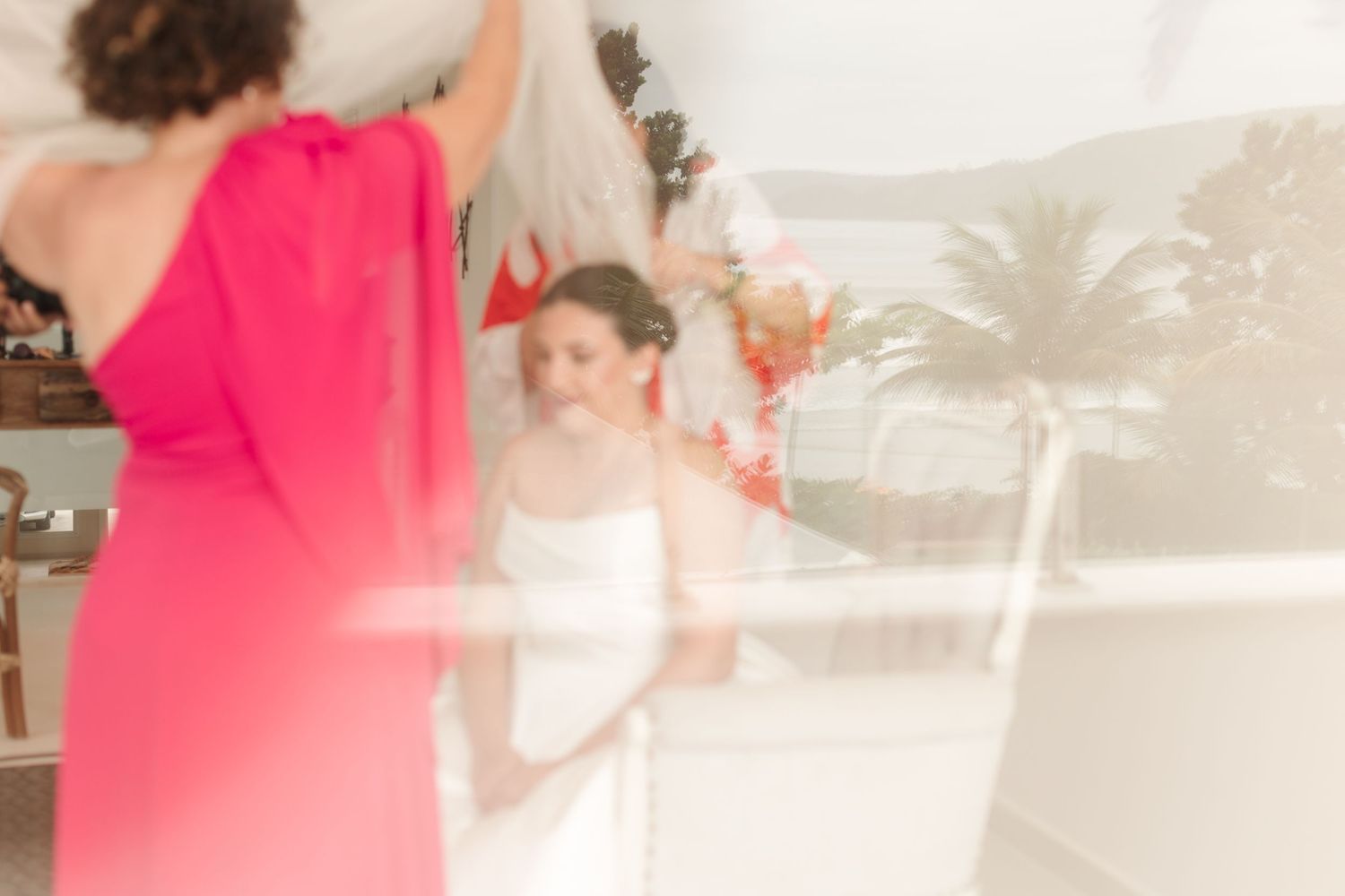 Artistic blurred wedding preparation scene with pink dress in foreground.