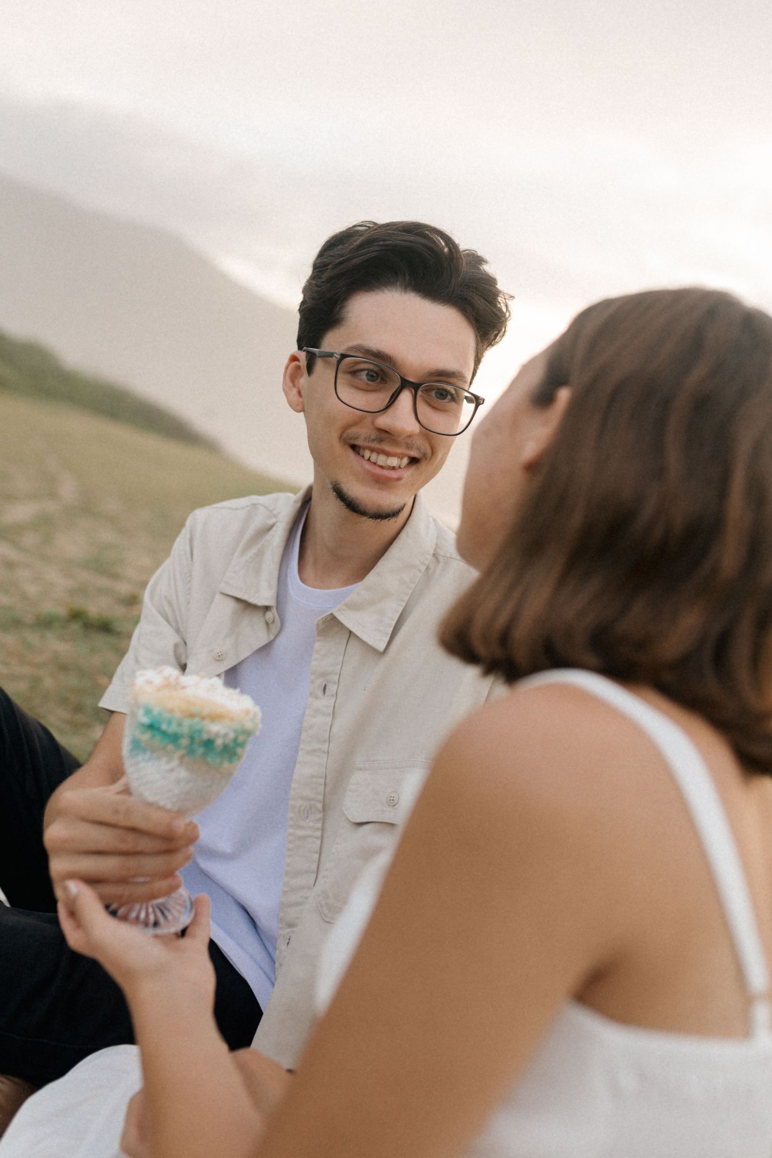 Romantic couple sharing intimate moments outdoors while enjoying desserts in a rustic natural setting at sunset.