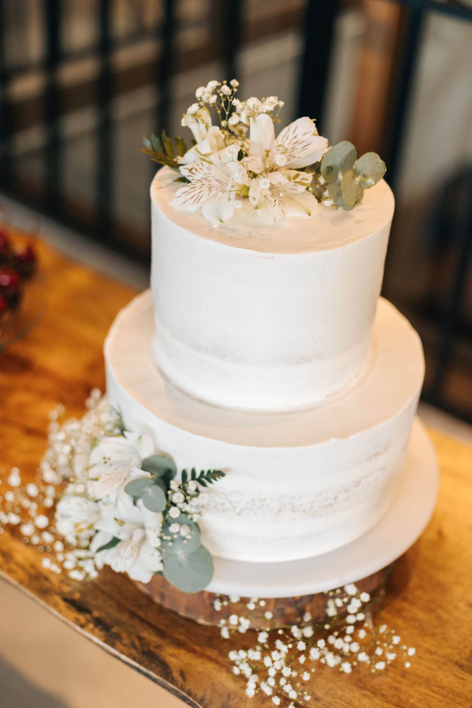 White two-tier wedding cake adorned with fresh flowers and baby's breath on wooden table.