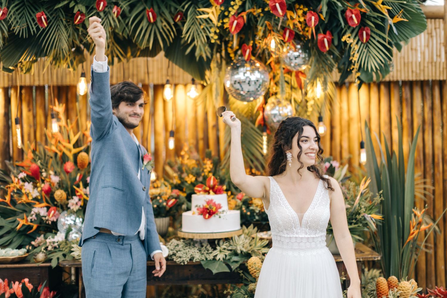 Newlyweds celebrate in front of tropical floral arch with wedding cake display.
