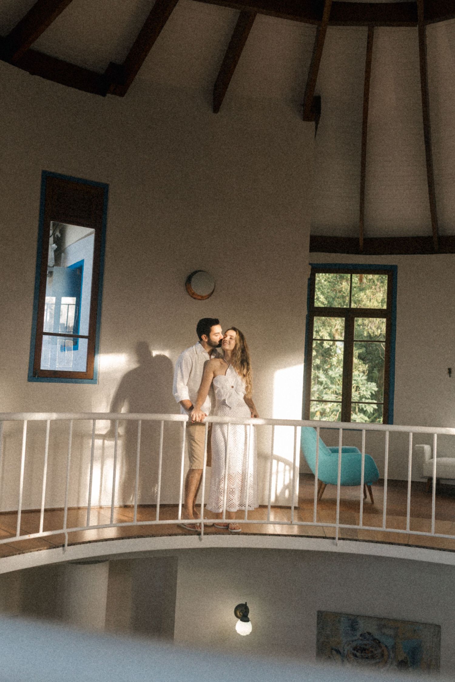 A couple stands together on a curved balcony in soft natural lighting.
