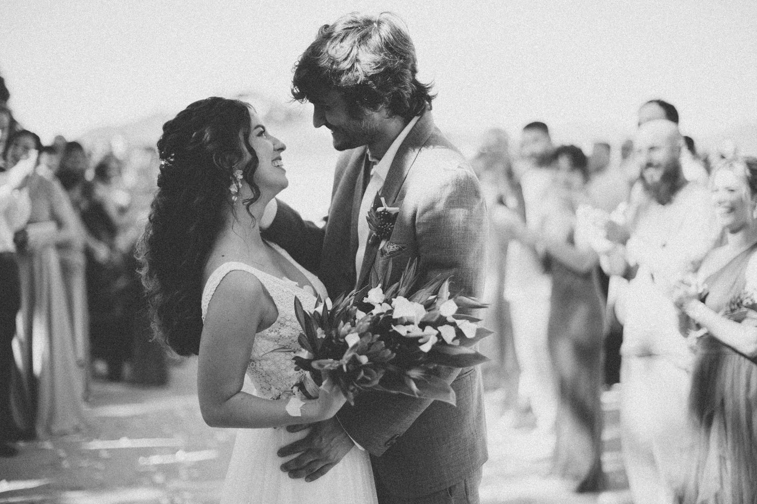 Black and white photo of a beach wedding recessional with guests celebrating.