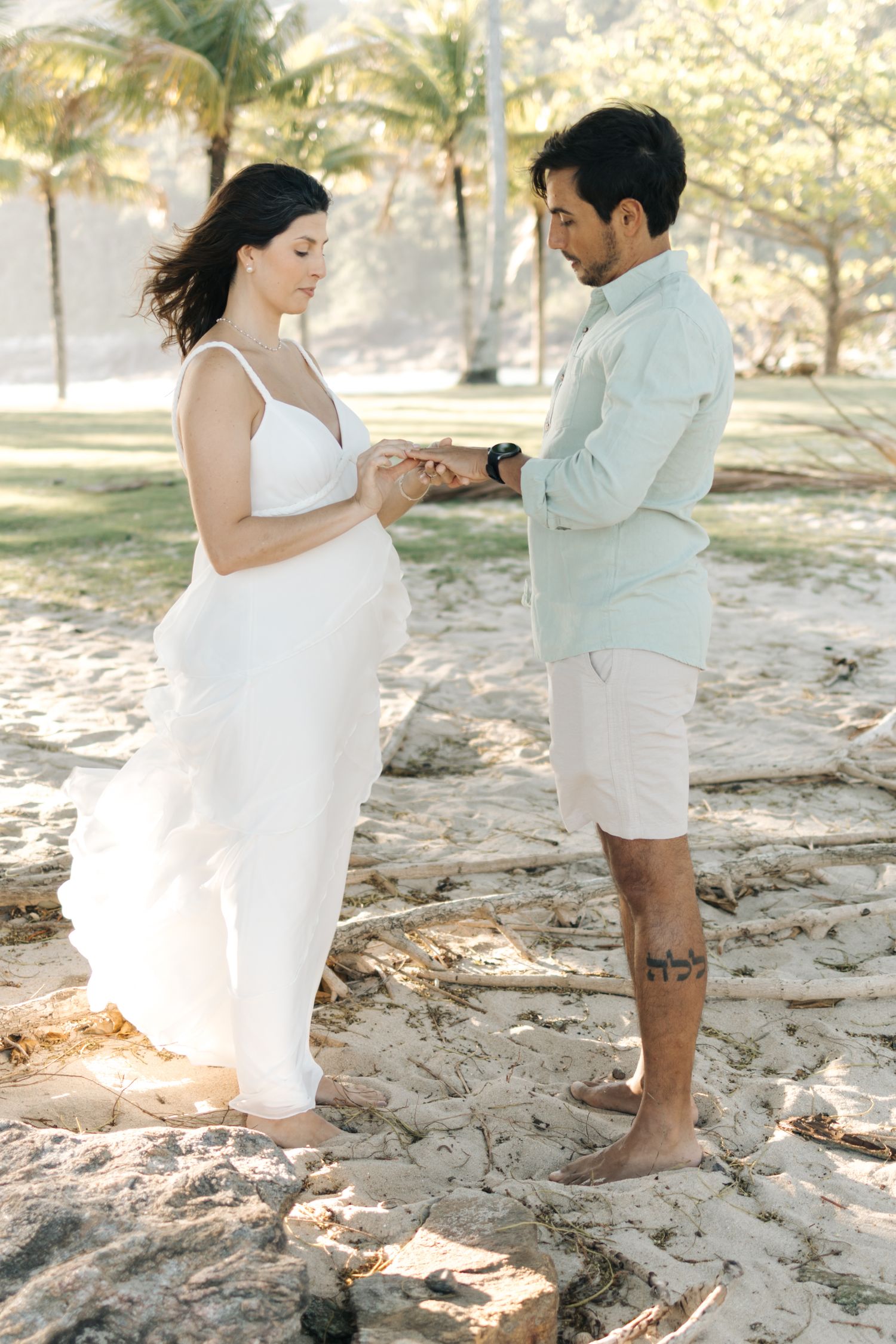 Romantic couple dancing together on a sandy beach with palm trees in the background.