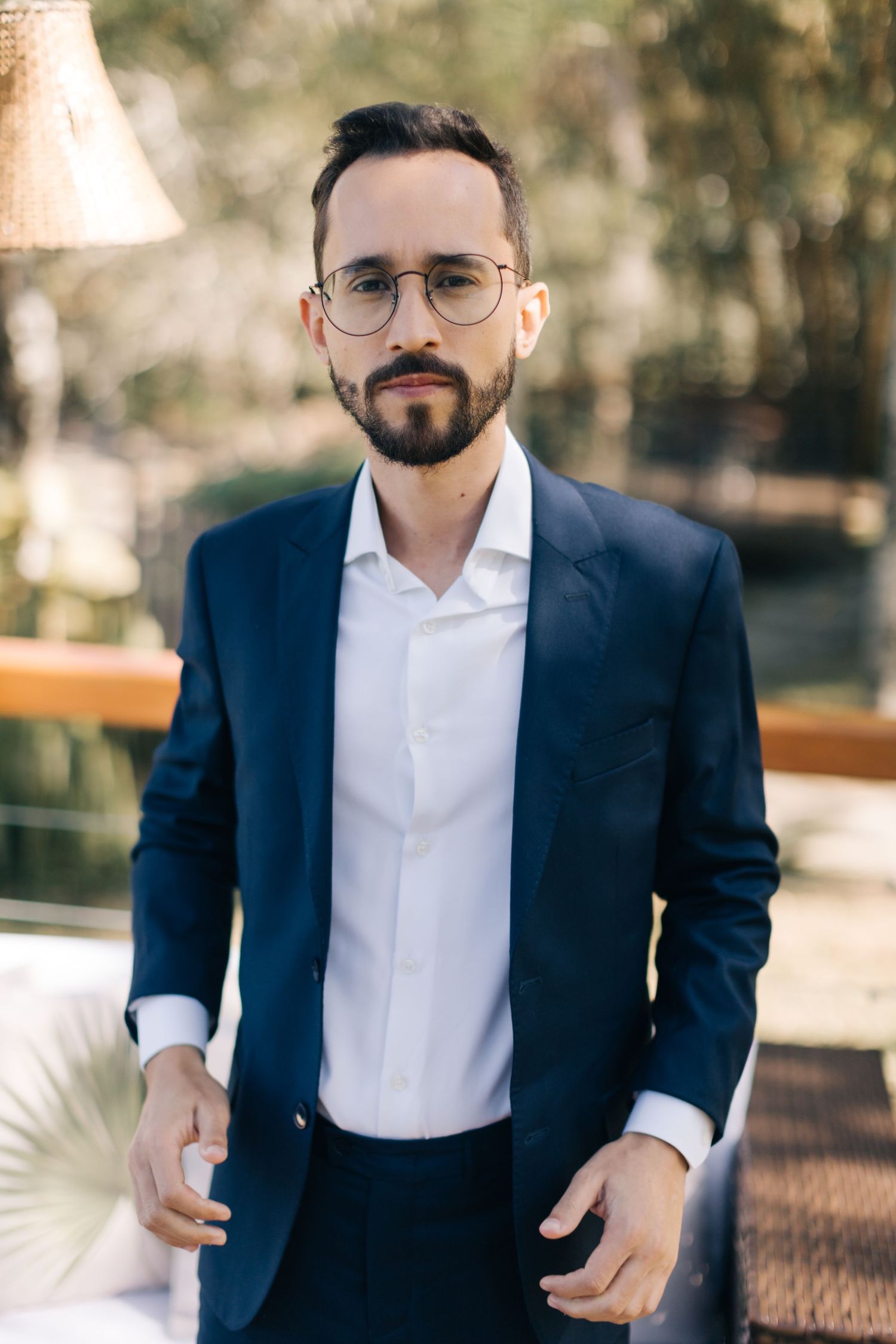 Professional wearing a navy suit jacket with glasses stands in natural outdoor lighting.