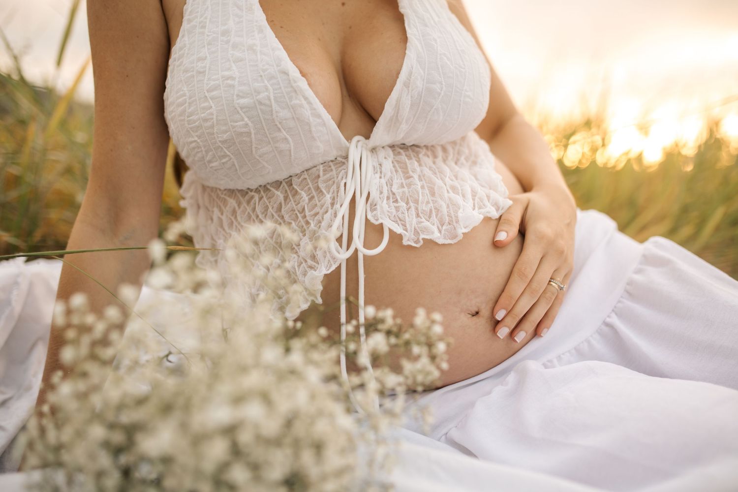 Maternity photoshoot in white lace dress among wildflowers at golden hour.