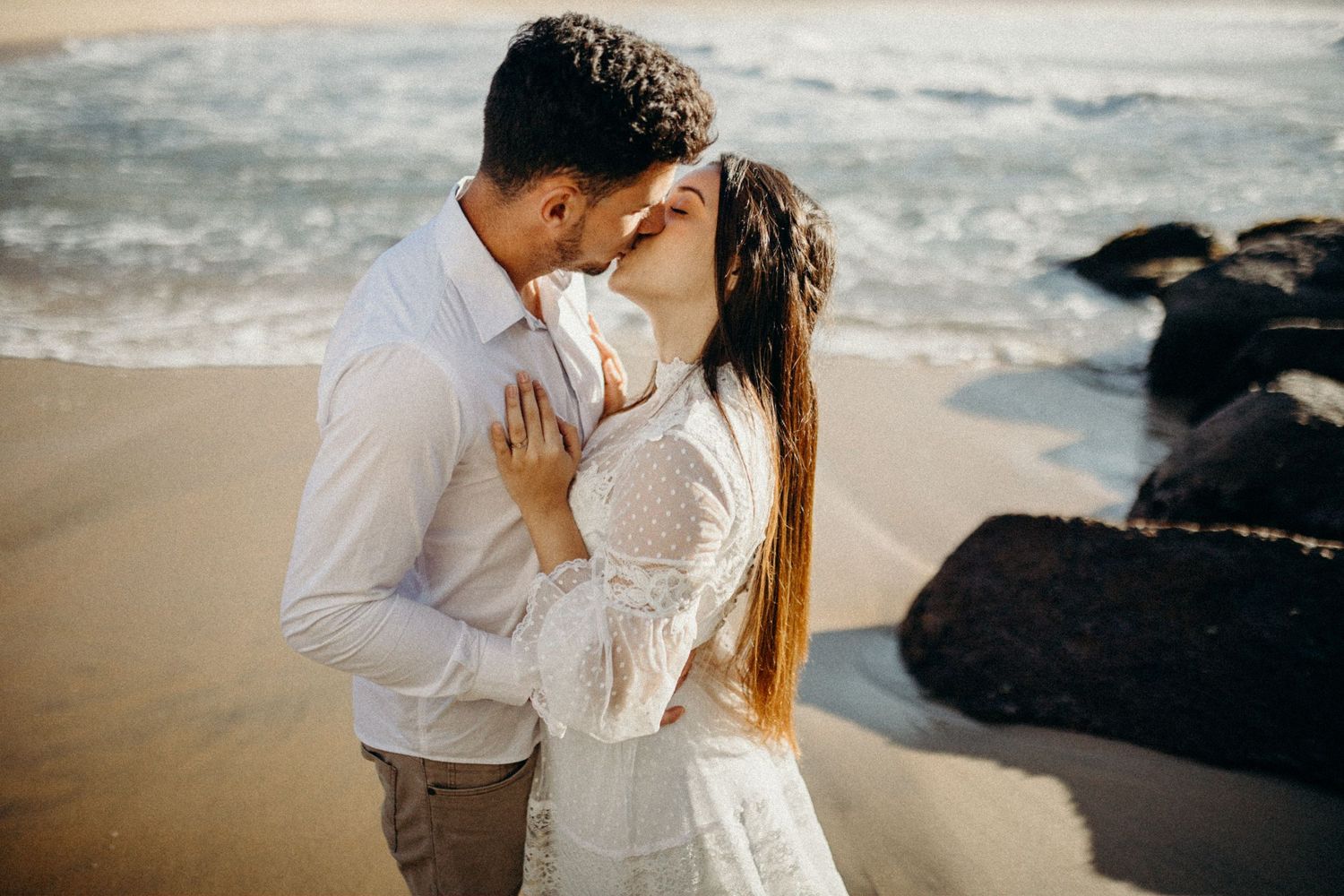 A romantic beachside embrace with ocean waves and dark rocks creating a dramatic scene.
