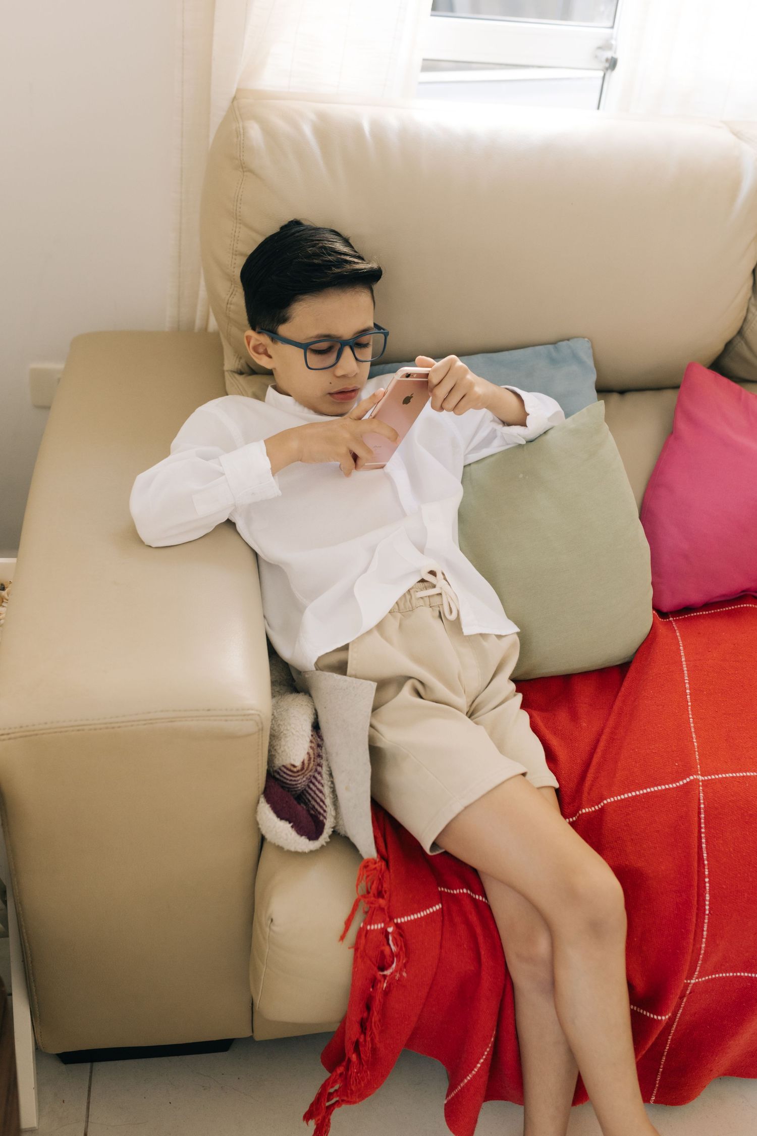 Person in white shirt and shorts relaxing on beige couch with colorful pillows.