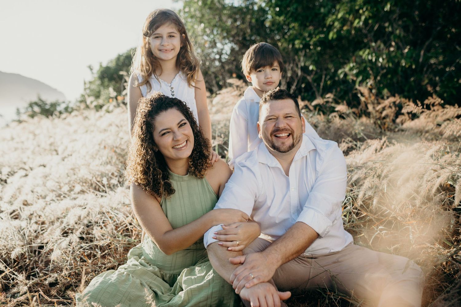 Natural light family portrait captured against mountain backdrop with everyone smiling together.