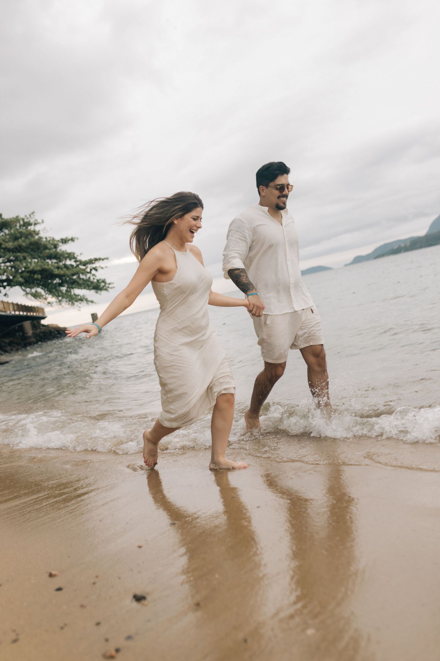 Two people playfully running through shallow water on a tropical beach.