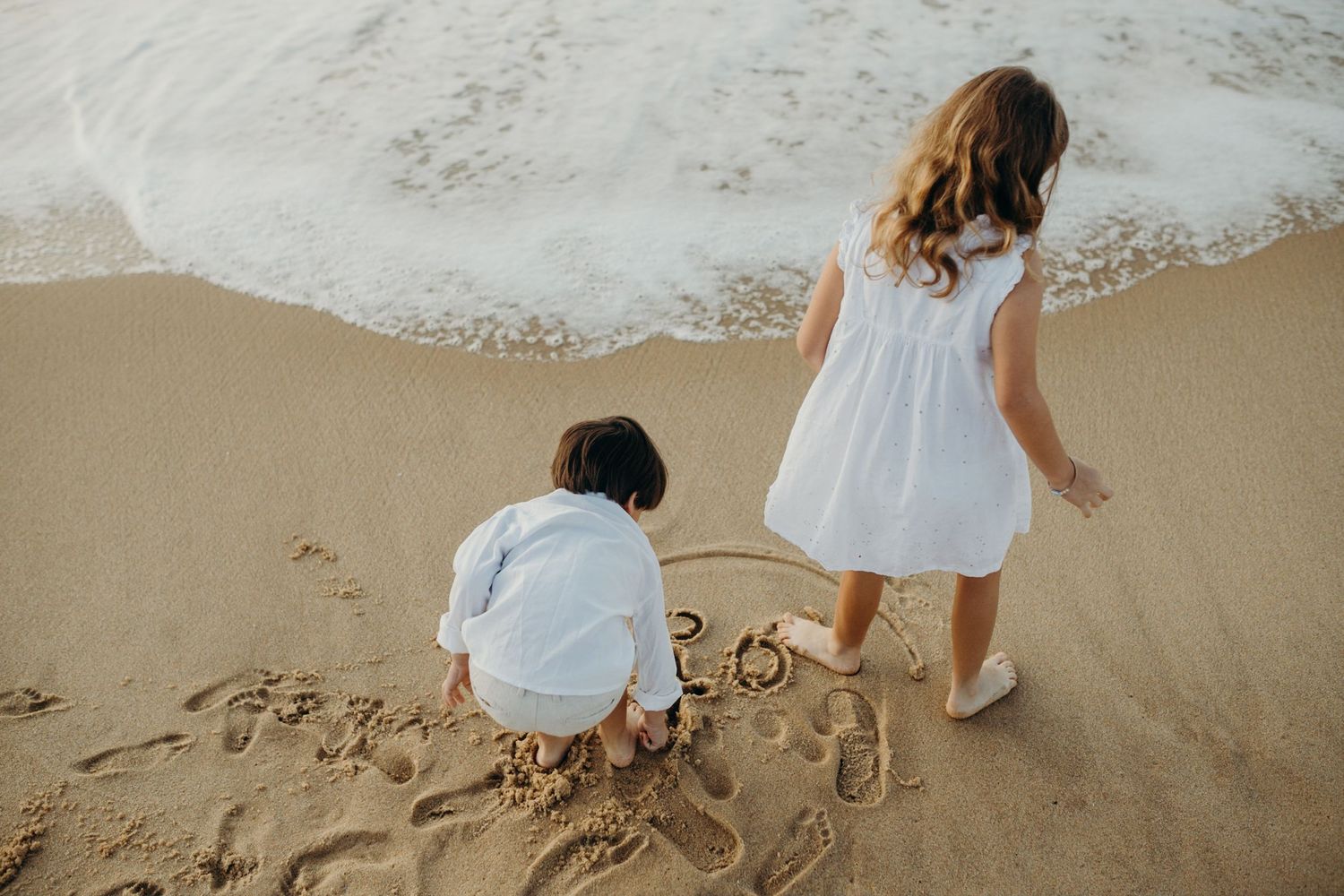 Children creating drawings in the sand at a scenic beach during golden hour.