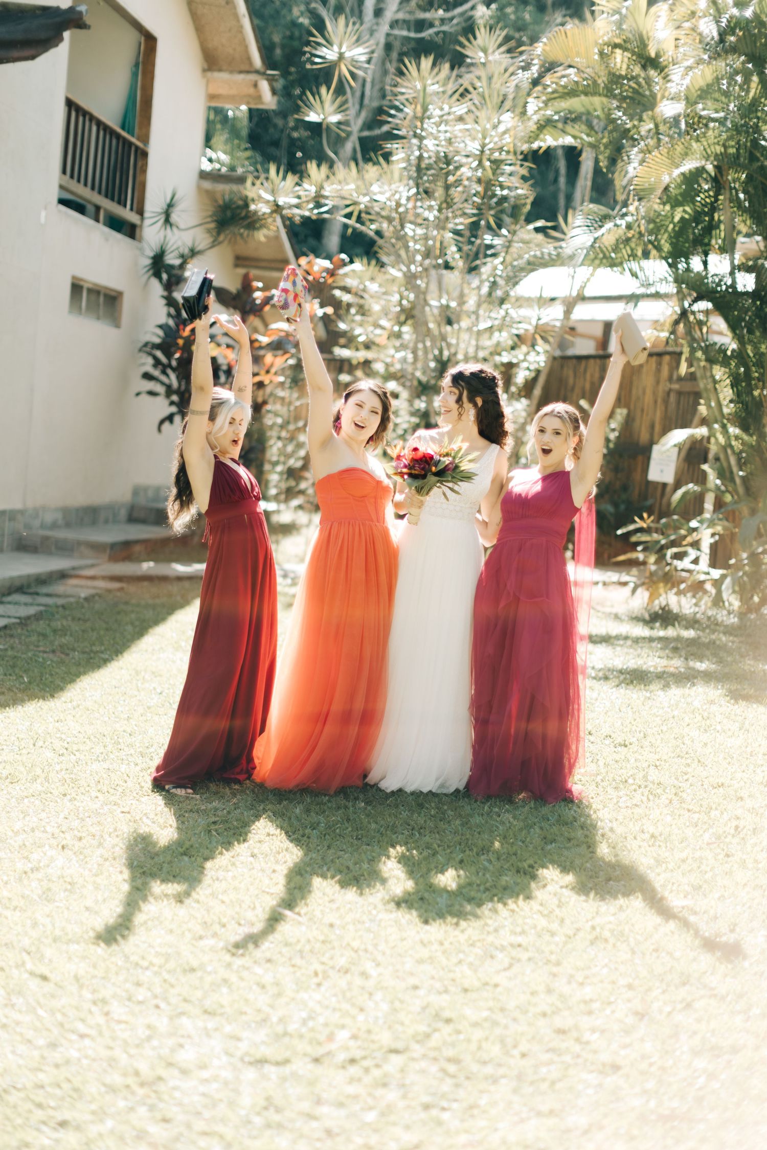 Bridesmaids in red and coral dresses celebrating joyfully with the bride outdoors.