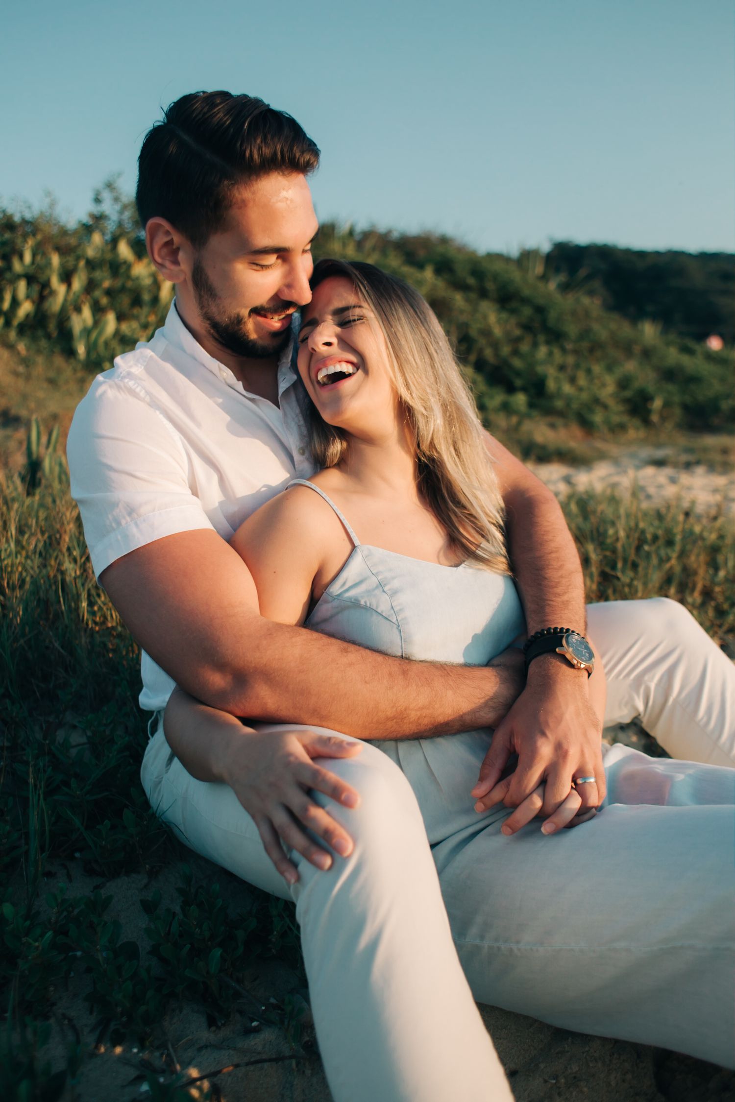 Happy couple laughing and embracing while wearing matching white outfits outdoors.
