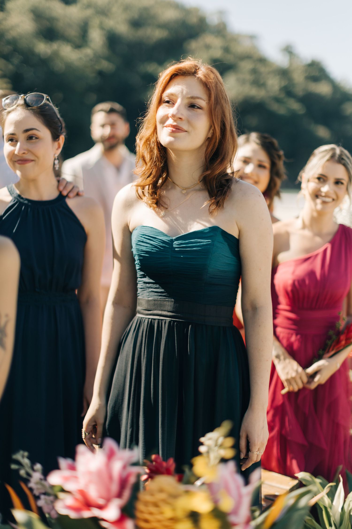 Bridesmaids stand in a line wearing elegant black and burgundy dresses at an outdoor ceremony.