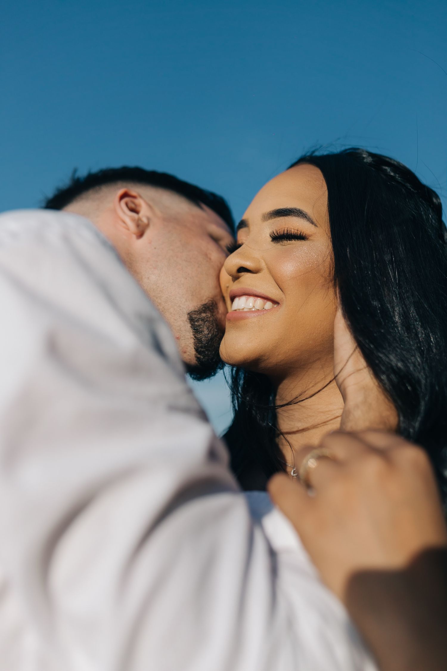 An intimate close-up portrait of a couple sharing a tender moment against blue sky.