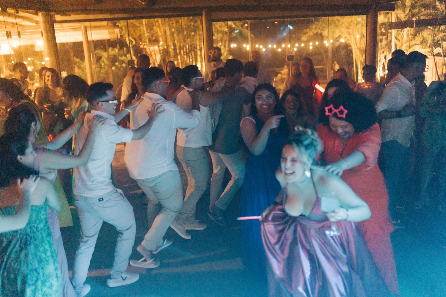 Large group of people dancing together at an outdoor evening celebration.