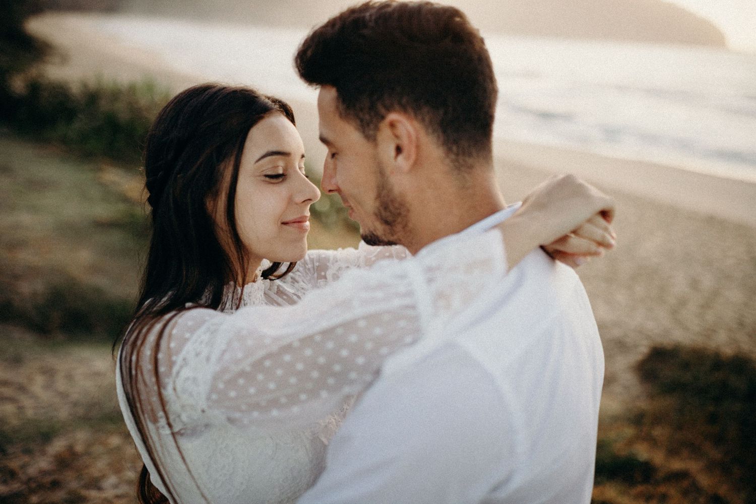 Couple sharing tender moment on coastal cliffs at sunset.
