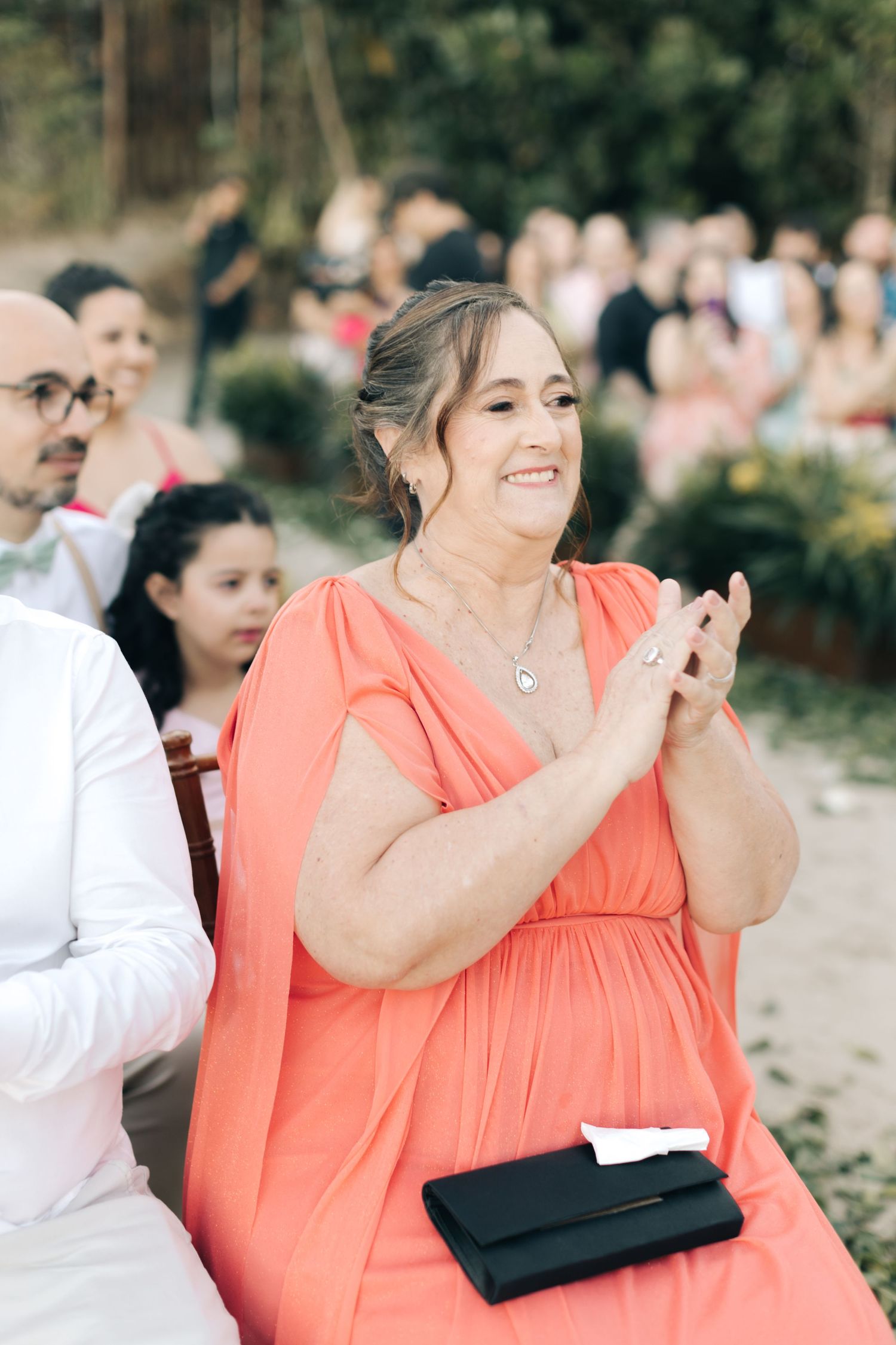 Wedding guests in coral dresses react emotionally during outdoor ceremony.