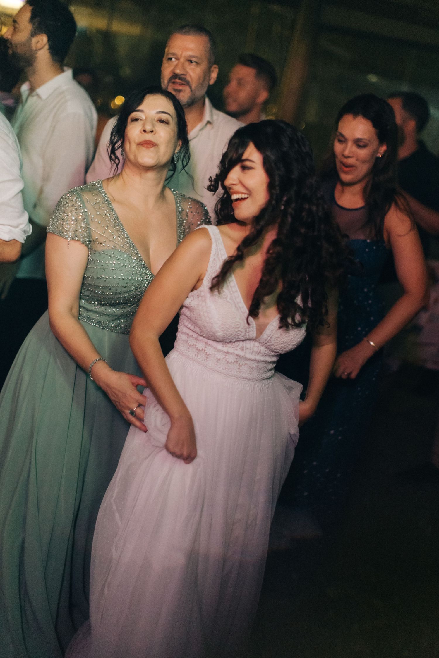 Wedding reception guests dancing and celebrating in formal attire under ambient lighting.