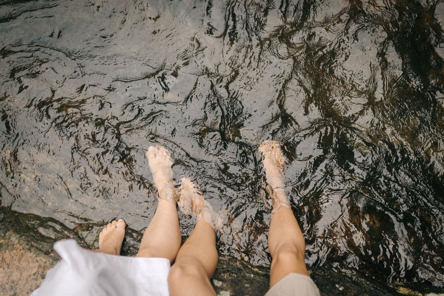 POV shot of bare feet on wet rocky terrain near water.
