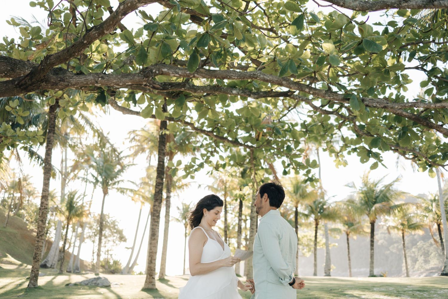 A couple shares a romantic moment under palm trees at sunset on a tropical beach.