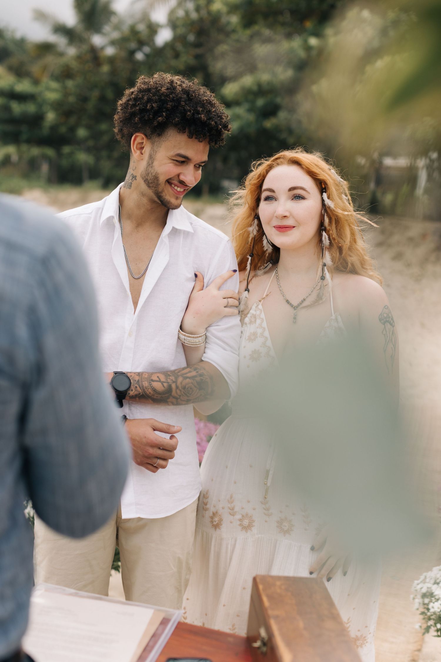 Couple in light summer attire sharing a tender moment during their beachside ceremony.