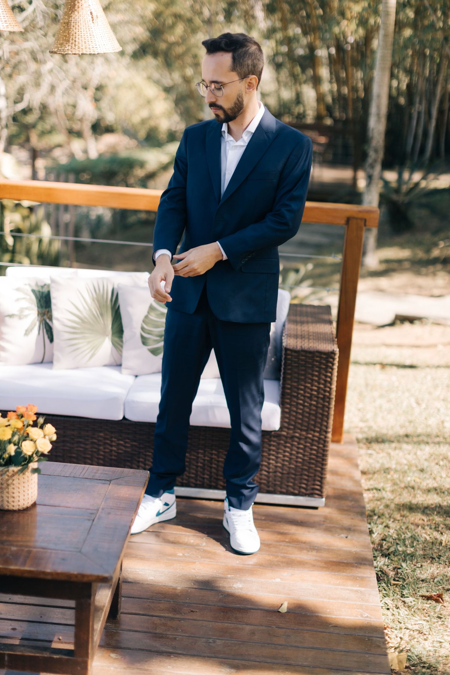 Groom in navy suit and white sneakers standing on wooden deck.