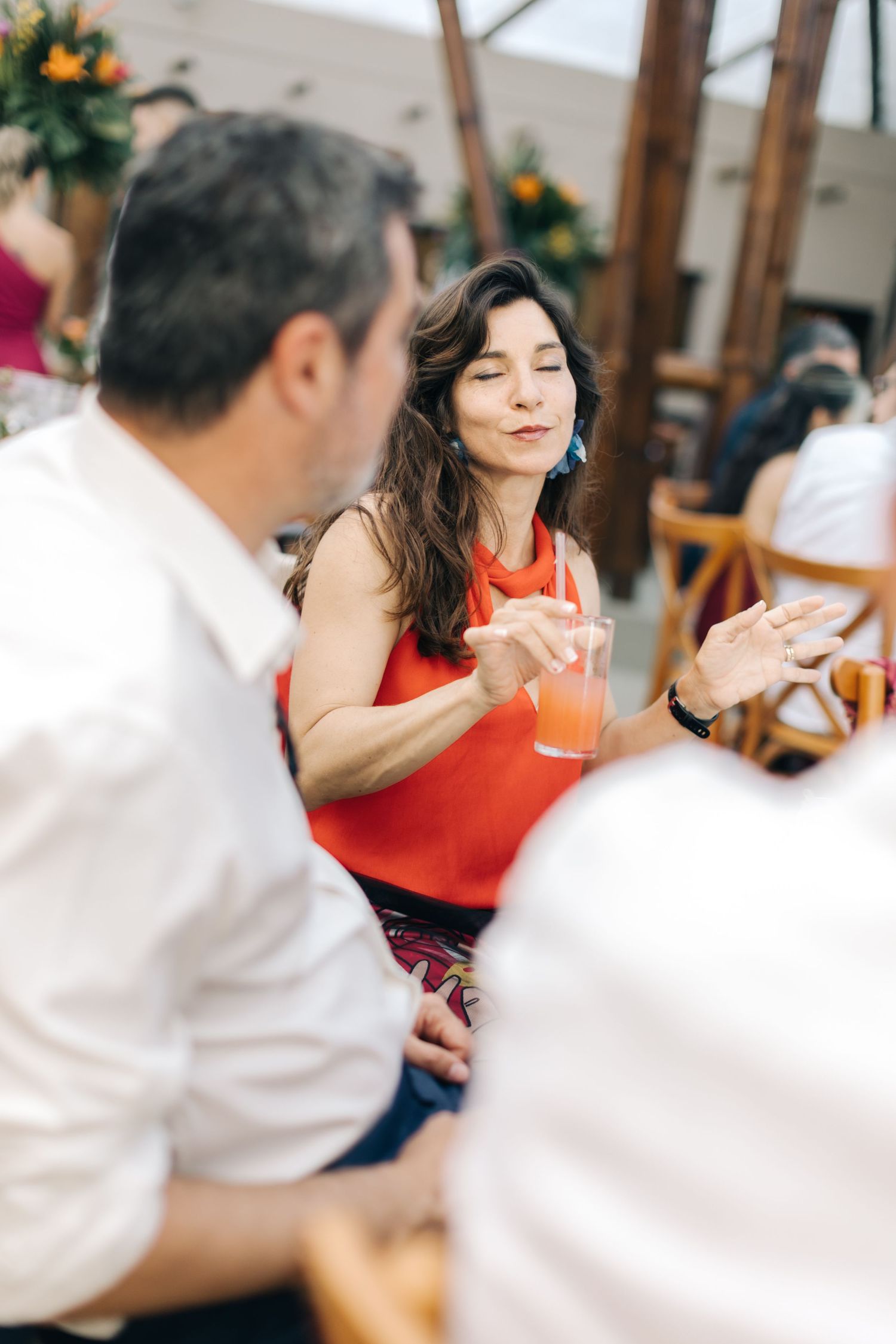Guest in vibrant red enjoying conversation at an outdoor wedding reception.