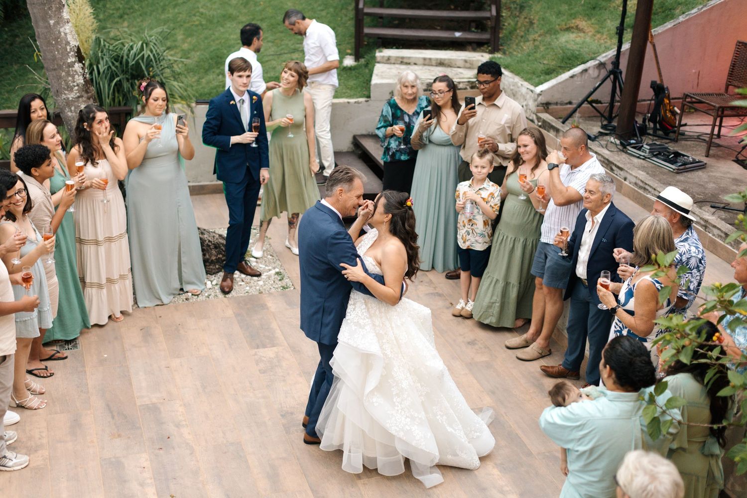 Wedding party and guests forming a celebratory receiving line outdoors with bridesmaids in sage green dresses.